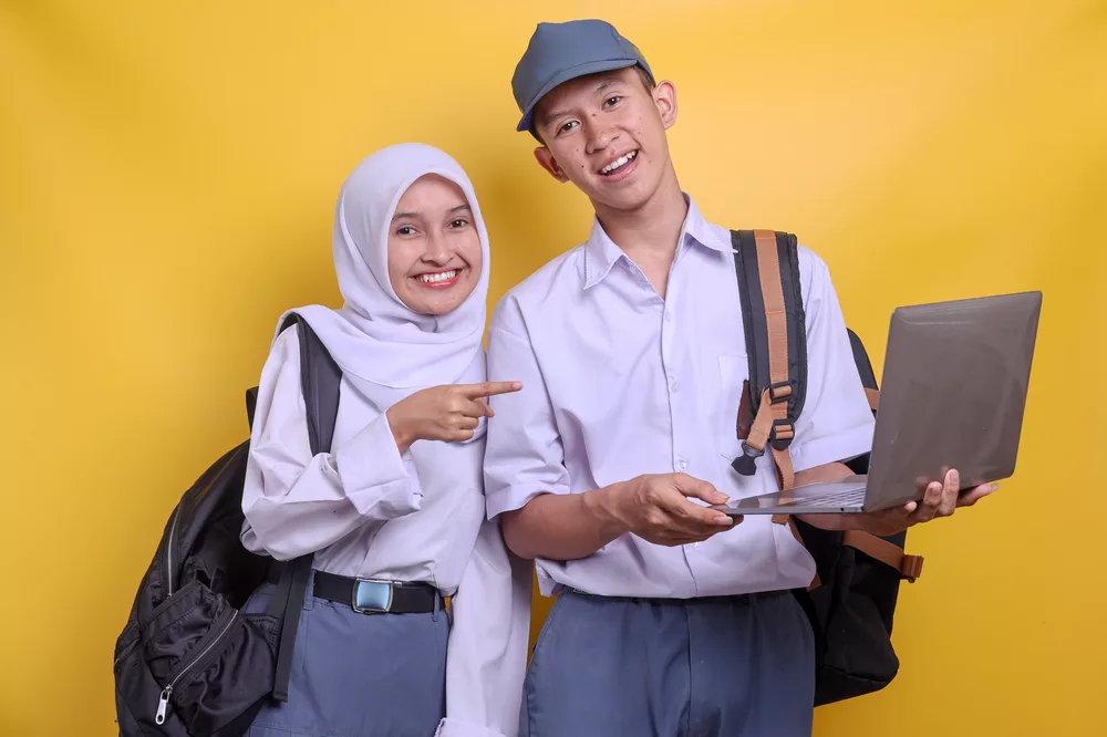 Dua siswa SMA berseragam sedang menggunakan laptop